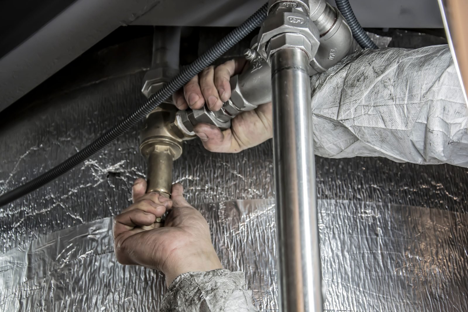Plumber's hands tightening a fitting on supply lines under a sink